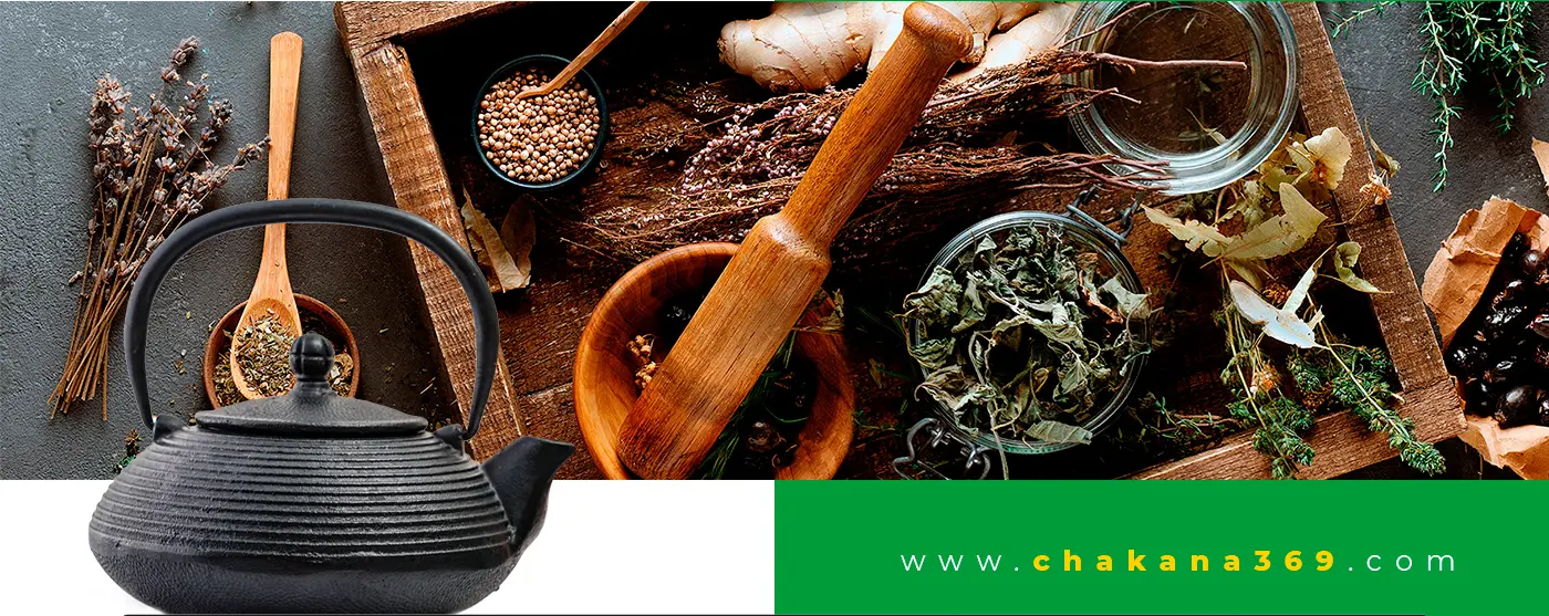 Cast-iron teapot next to dried herbs and spices on wood