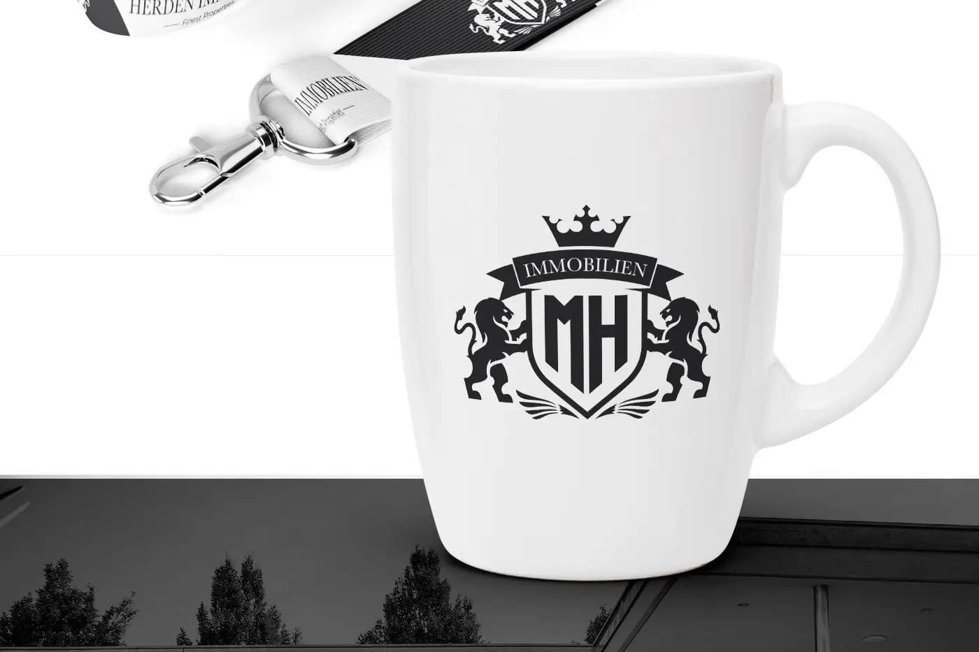 Taza blanca con el escudo de Herden Immobilien junto a una cinta identificativa