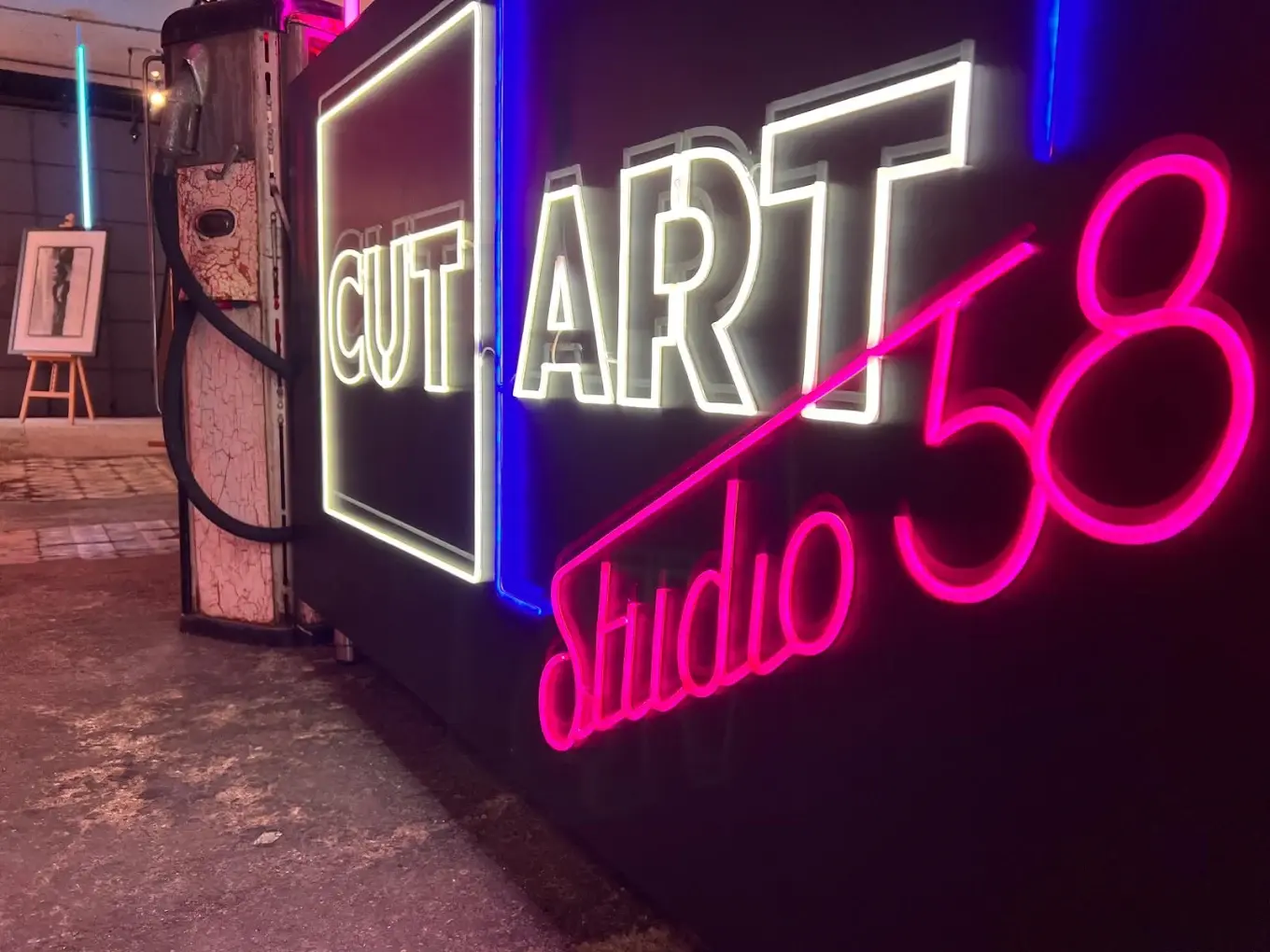 Rótulo de neón CUT ART Studio 58 encendido en el local, junto a un surtidor antiguo