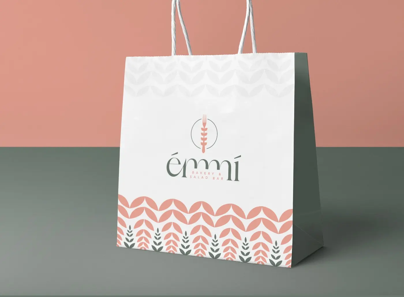White paper bag with the Émmí logo and a leaf print in coral and green