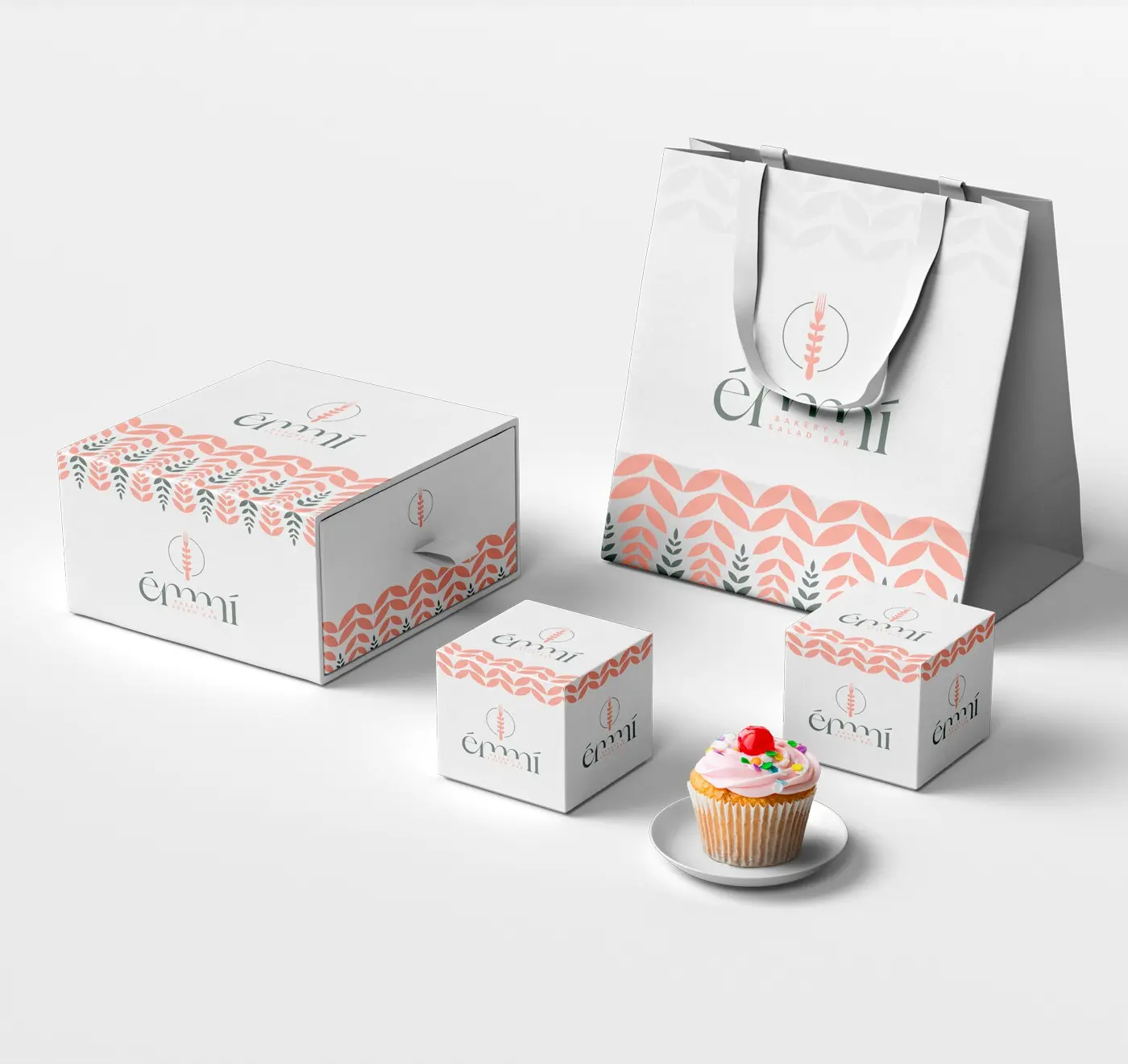 Émmí packaging boxes and bag next to a cupcake with cream and colourful cherries
