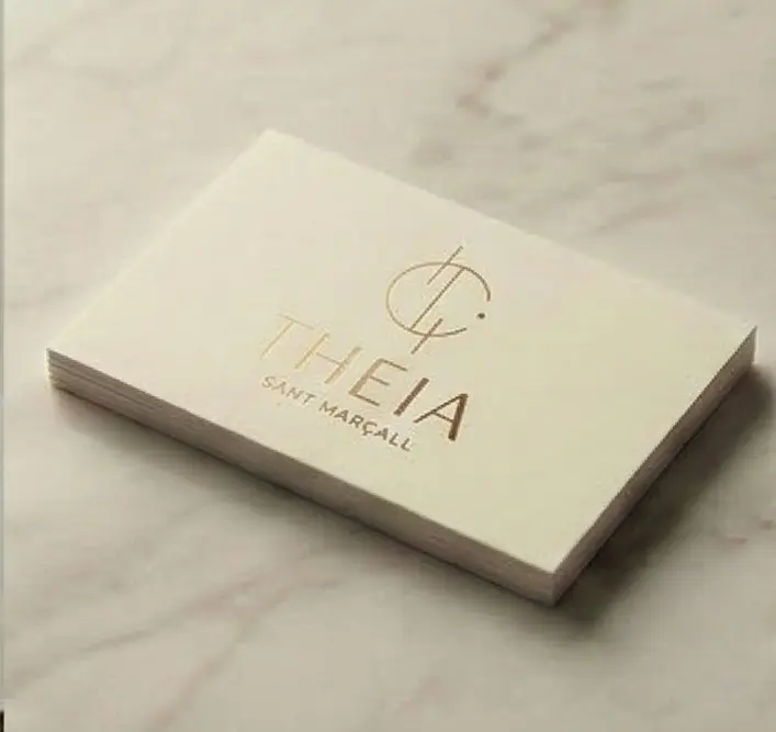 Tarjeta de visita con el logotipo de Theia estampado en dorado sobre papel crema