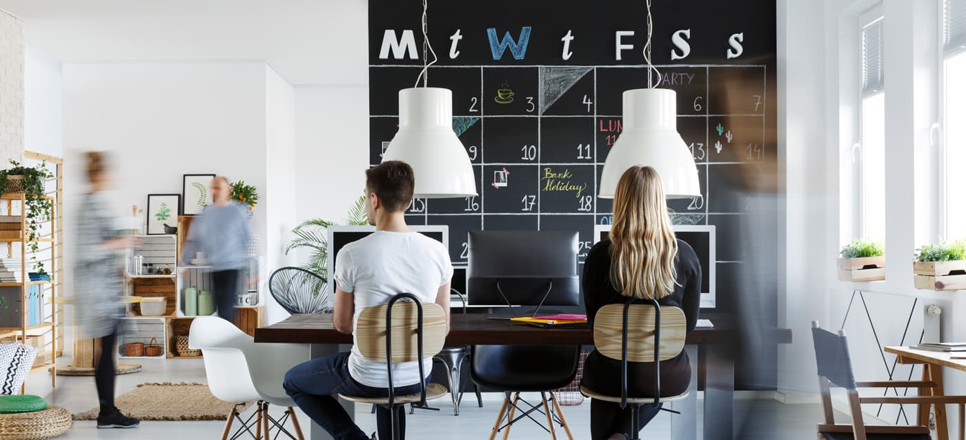 Fotografía de un espacio de coworking con mesas compartidas y una pizarra tipo calendario