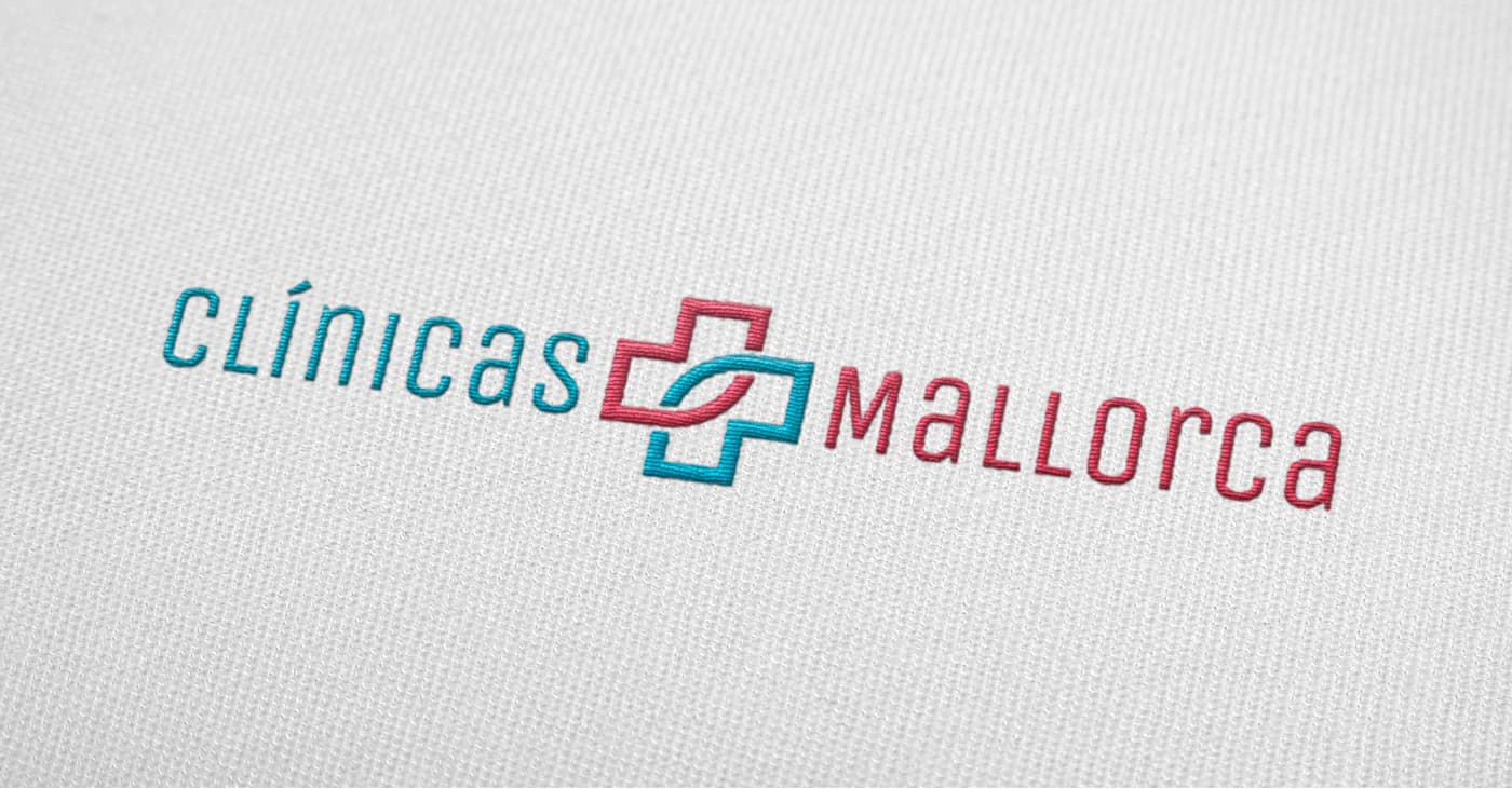Logotipo de Clínicas Mallorca bordado en azul y coral sobre tela blanca