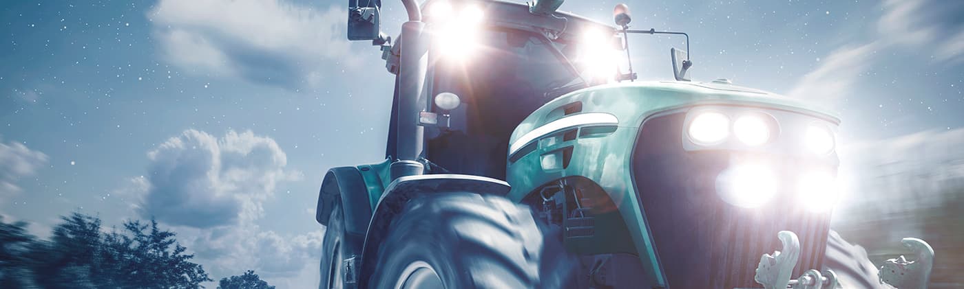 Fotografía de un tractor verde circulando de noche con los faros encendidos