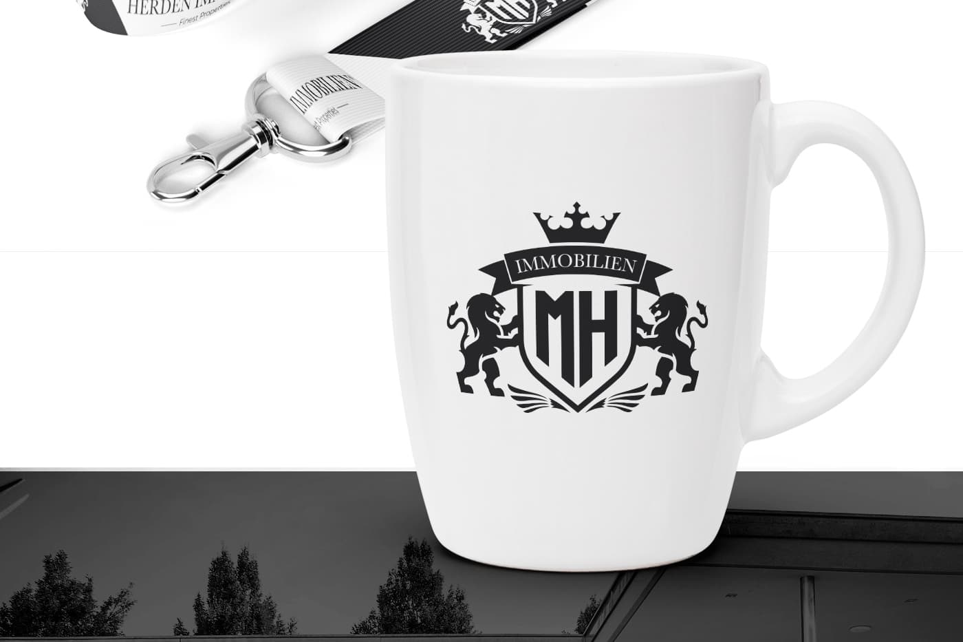 Taza blanca con el escudo de Herden Immobilien junto a una cinta identificativa