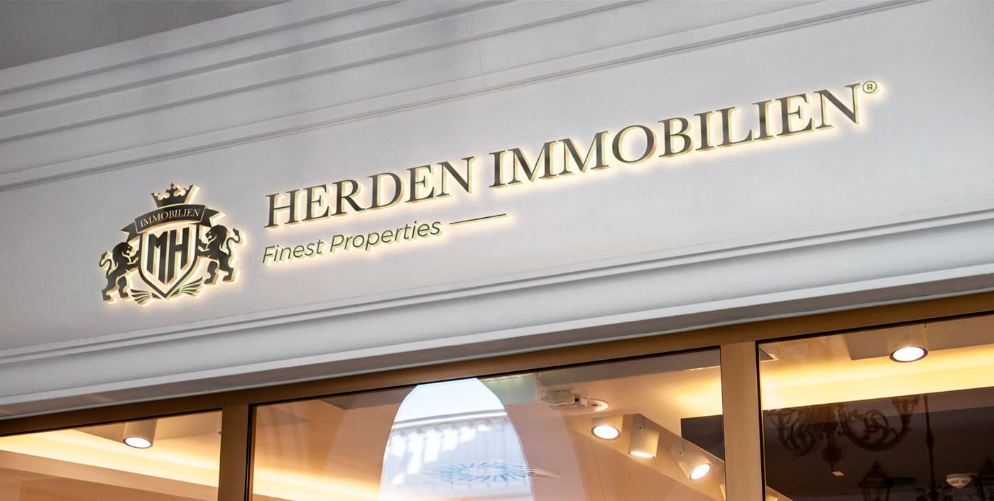 Rótulo iluminado de Herden Immobilien en la fachada de la oficina inmobiliaria