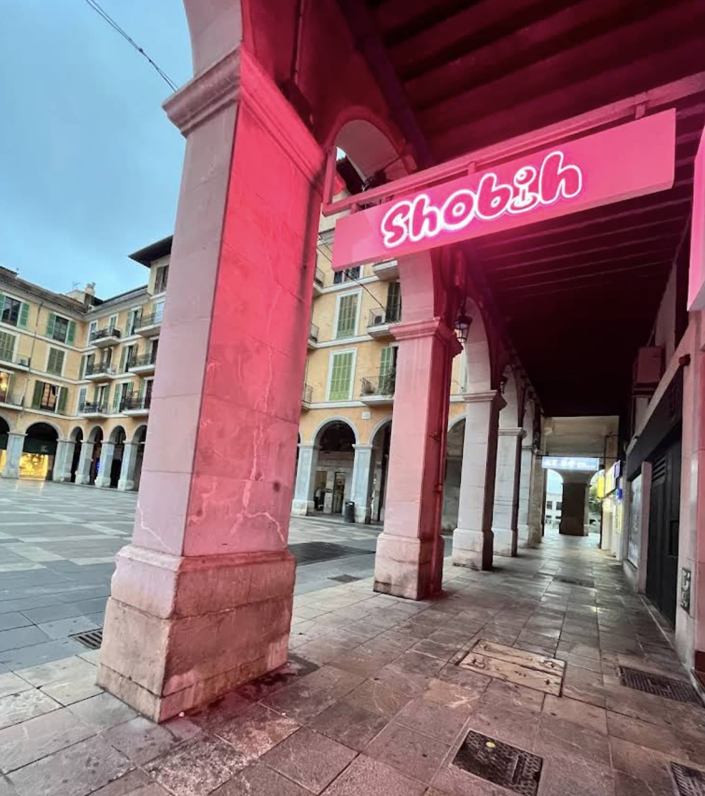 Rótulo de neón rosa de Shobih bajo los arcos de una plaza histórica