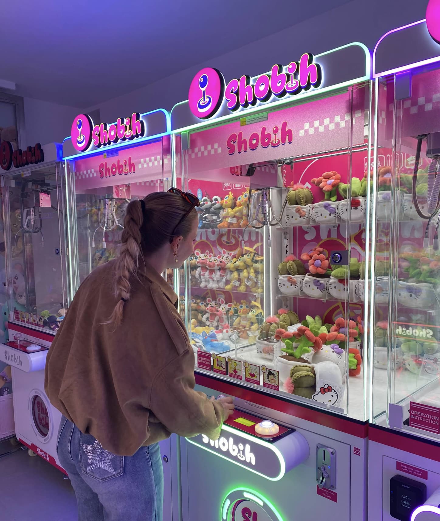 Mujer jugando en una máquina de peluches rosa iluminada con neón
