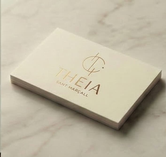 Targeta de visita amb el logotip de Theia estampat en daurat sobre paper crema